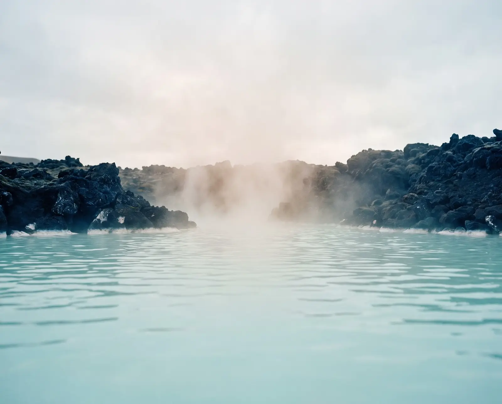 Aguas turquesa lechosas y vapor entre rocas de lava negra